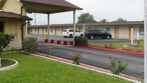 A motel with a covered parking area, a grassy lawn, and a red curb.