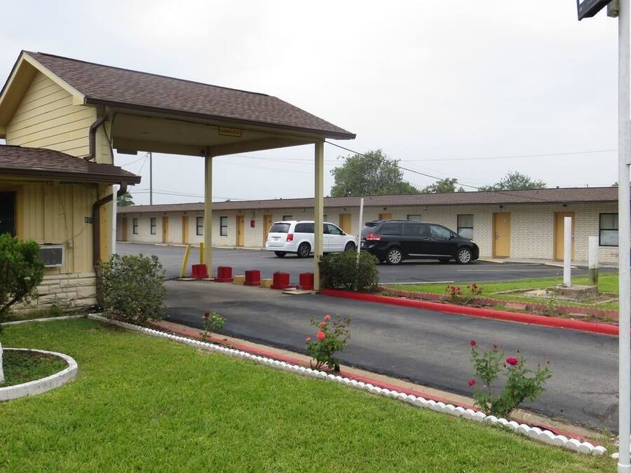 A motel with a covered parking area, a grassy lawn, and a red curb.