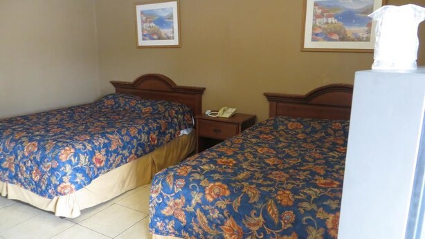 A hotel room with two beds, each with floral-patterned bedding, a nightstand with a telephone, and a wall-mounted painting.
