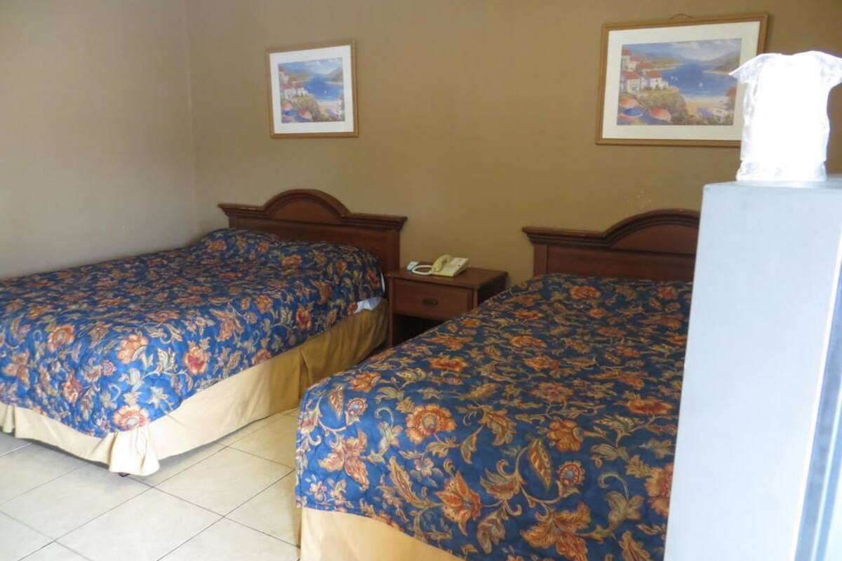 Une chambre d’hôtel avec deux lits, chacun agrémenté de draps à motifs floraux, une table de chevet avec un téléphone et un tableau accroché au mur.