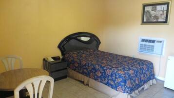 A small, single-room hotel room with a bed, a desk, and a chair.