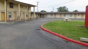 A motel with a row of single-story rooms, a parking lot, and a small grassy area with a chair.