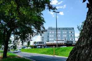 Um hotel com uma placa indicando "Vitoria Régia Hotel" e uma estrada visível com carros.