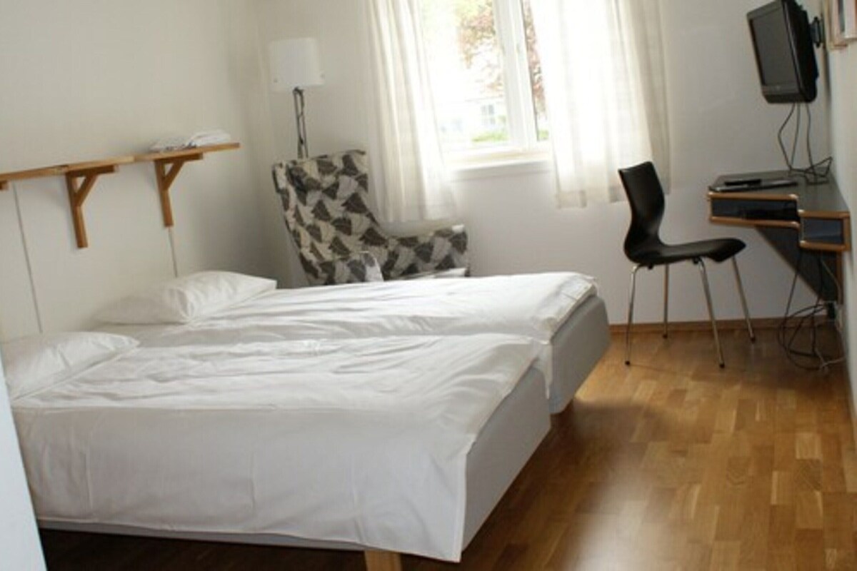 A hotel room with a bed, a desk with a computer, a chair, and a window with curtains.