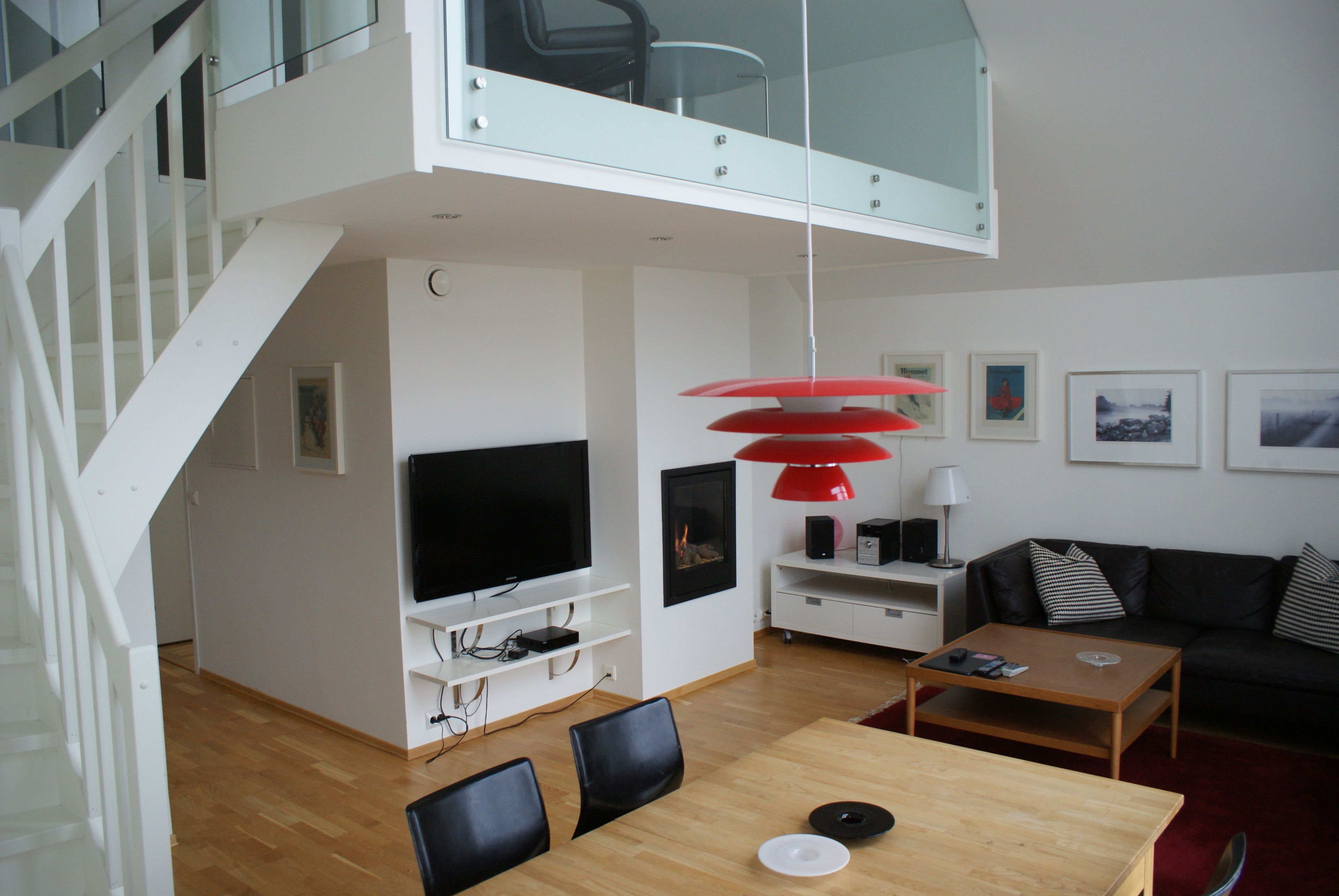 Una sala de estar moderna con televisor, lámpara colgante roja y sofá de cuero negro.