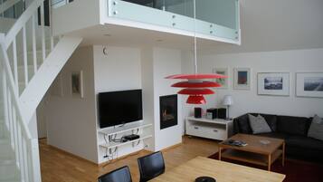 Una sala de estar moderna con televisor, lámpara colgante roja y sofá de cuero negro.