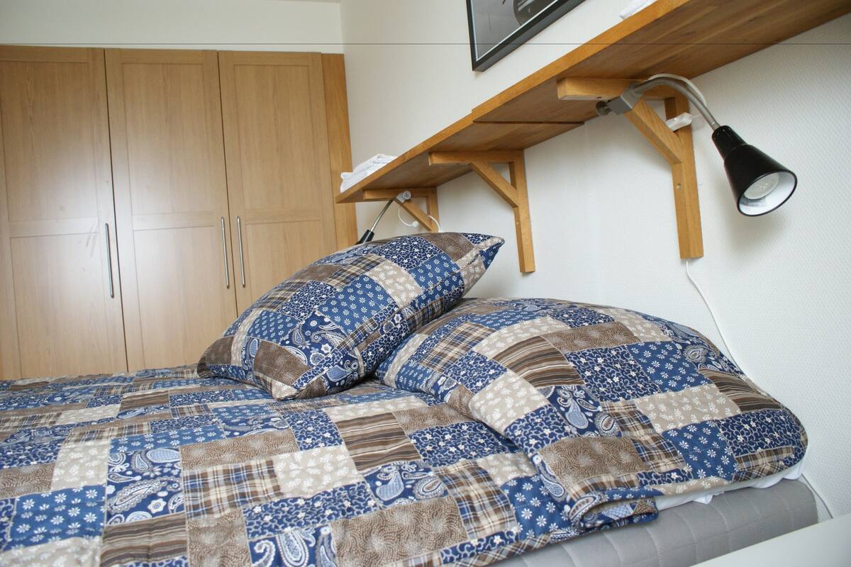 Ein Bett mit Patchworkdecke, ein Holzschrank und ein Schreibtisch mit Lampe.