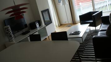 A modern living room with a flat-screen TV, a white table, black chairs, a black sofa, and a striped rug.