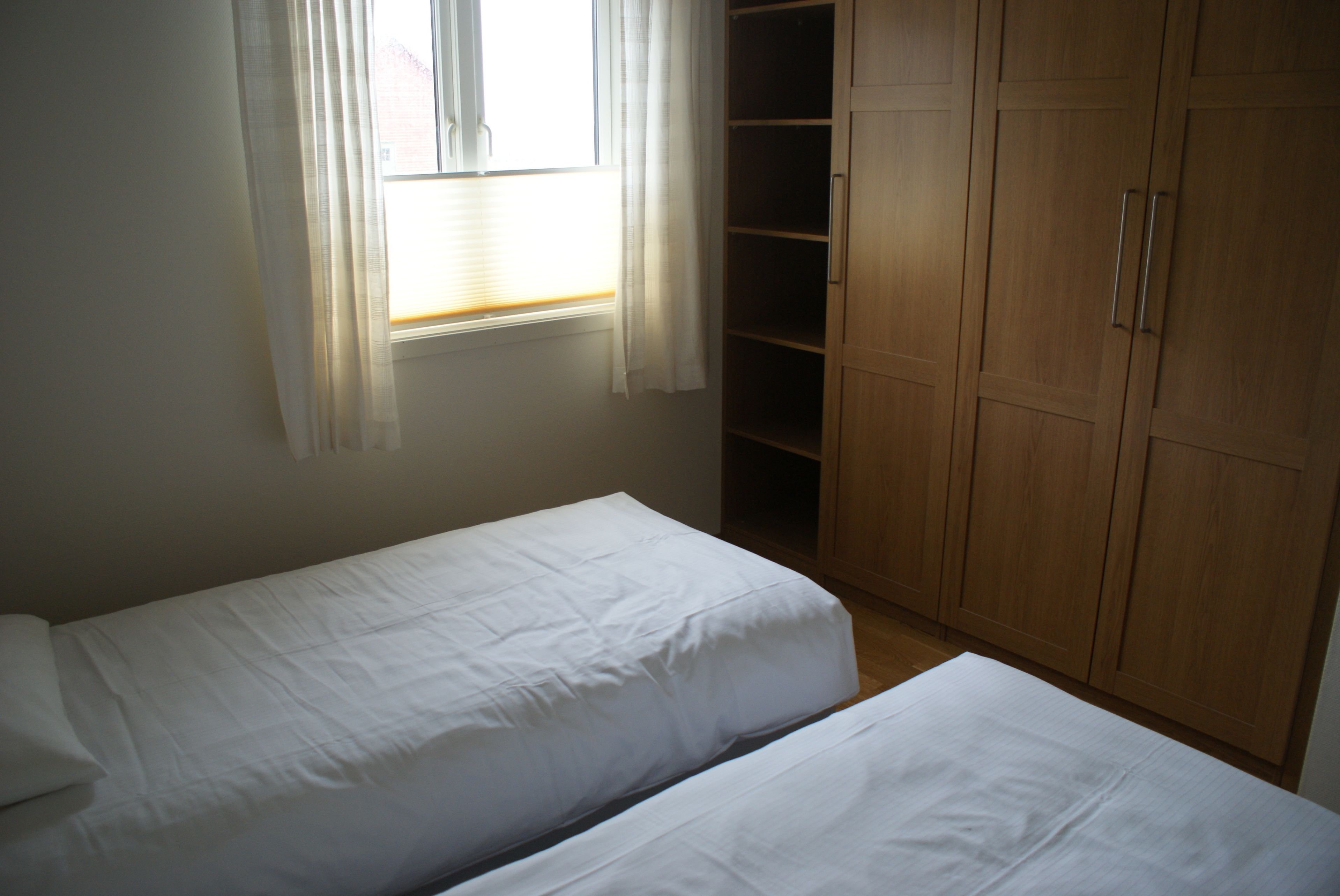 A bedroom with two single beds, a wooden wardrobe, and a window with curtains.