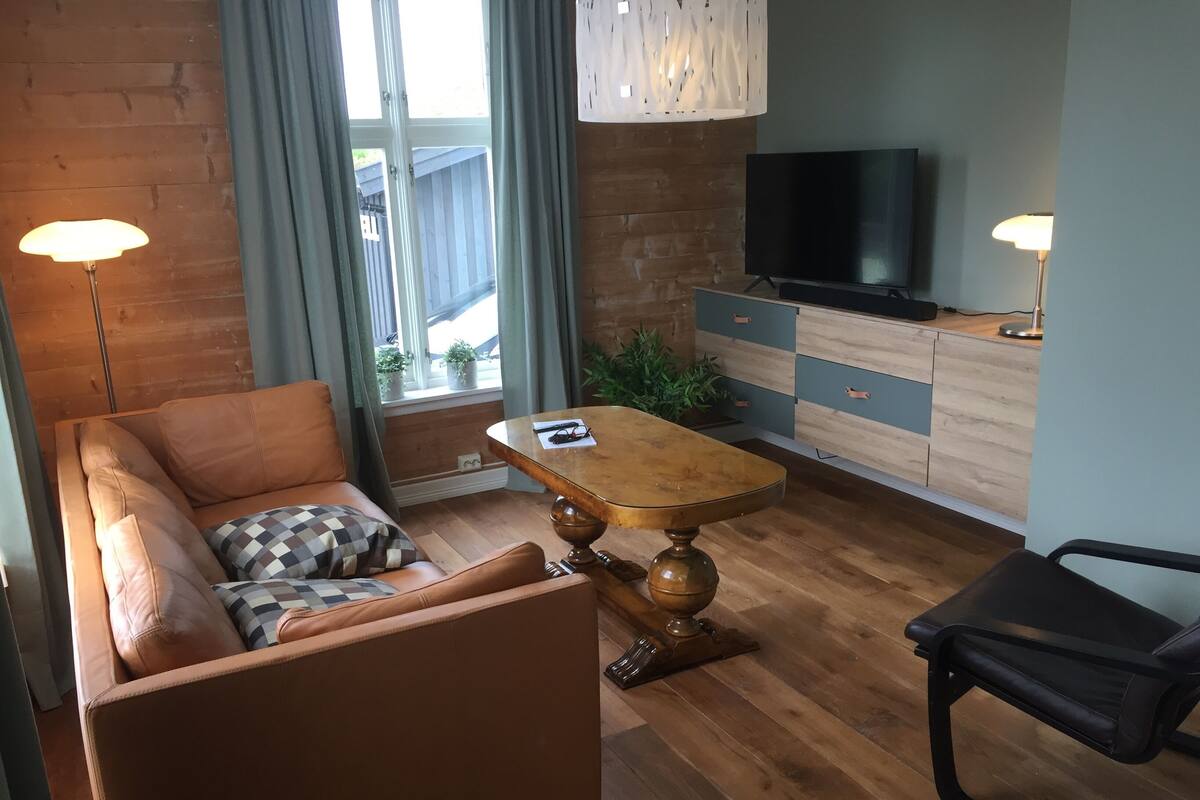 Ein modernes Wohnzimmer mit einer Couch, einem Holztisch, einem Fernseher und einem Schreibtisch mit Schubladen.