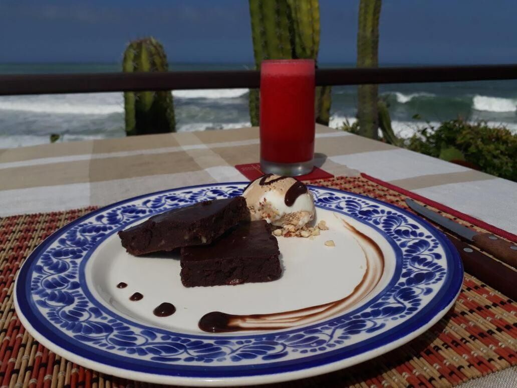 A dessert plate with chocolate brownies and ice cream on a blue and white patterned plate, with a red drink in the background.