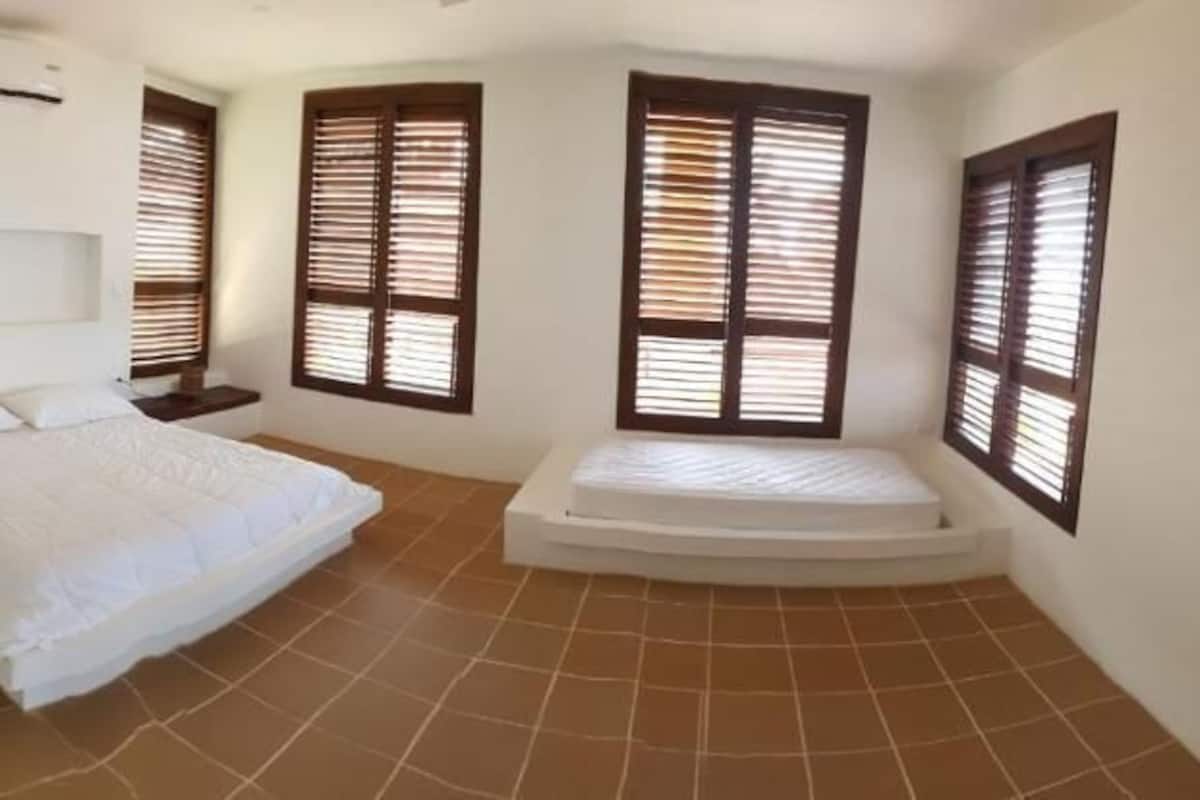 Un dormitorio con cama, mesita de noche, ventana con persianas y aire acondicionado instalado en la pared.