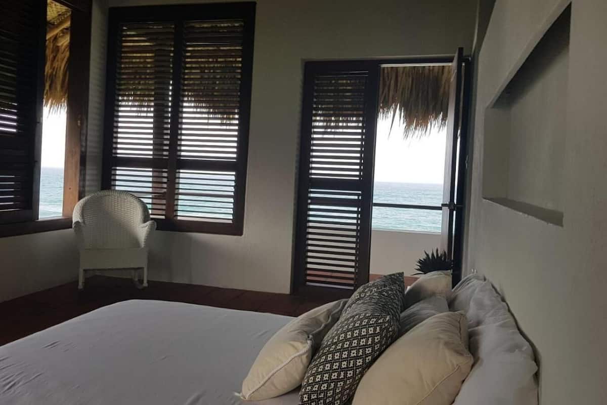 Un dormitorio con cama, una silla y vistas al mar a través de contraventanas abiertas.