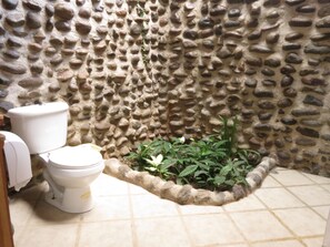 A bathroom with a stone wall, a toilet, and a small planter with plants.