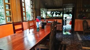 Un comedor de madera con una mesa larga y bancos, un florero con flores, y vistas al exterior a través de amplias ventanas.