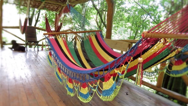 Una hamaca colgada en una terraza de madera con vista a árboles.