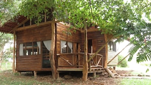 Una cabaña de madera con un porche, rodeada de árboles y un jardín.