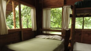 Una habitación de cabaña de madera con una cama, un banco y ventanas grandes con cortinas.