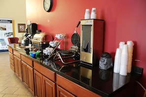 A kitchen area with a coffee machine, waffle maker, and various containers. - Edgewood Hotel & Suites (Fairbury)