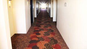A hotel hallway with a patterned carpet, doors on both sides, and a light at the end. - Edgewood Hotel & Suites (Fairbury)