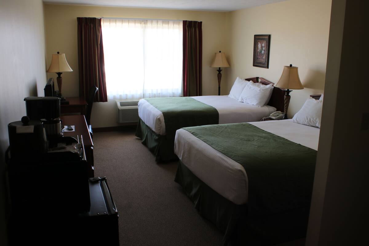 A hotel room with two beds, a desk, a chair, a coffee maker, and two lamps.