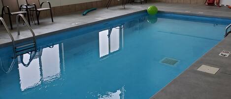 An indoor swimming pool with clear water, a green ball, and a sign about pool regulations.