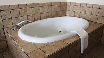 A white freestanding bathtub with a single faucet, set against a tiled wall with a brown and beige pattern.