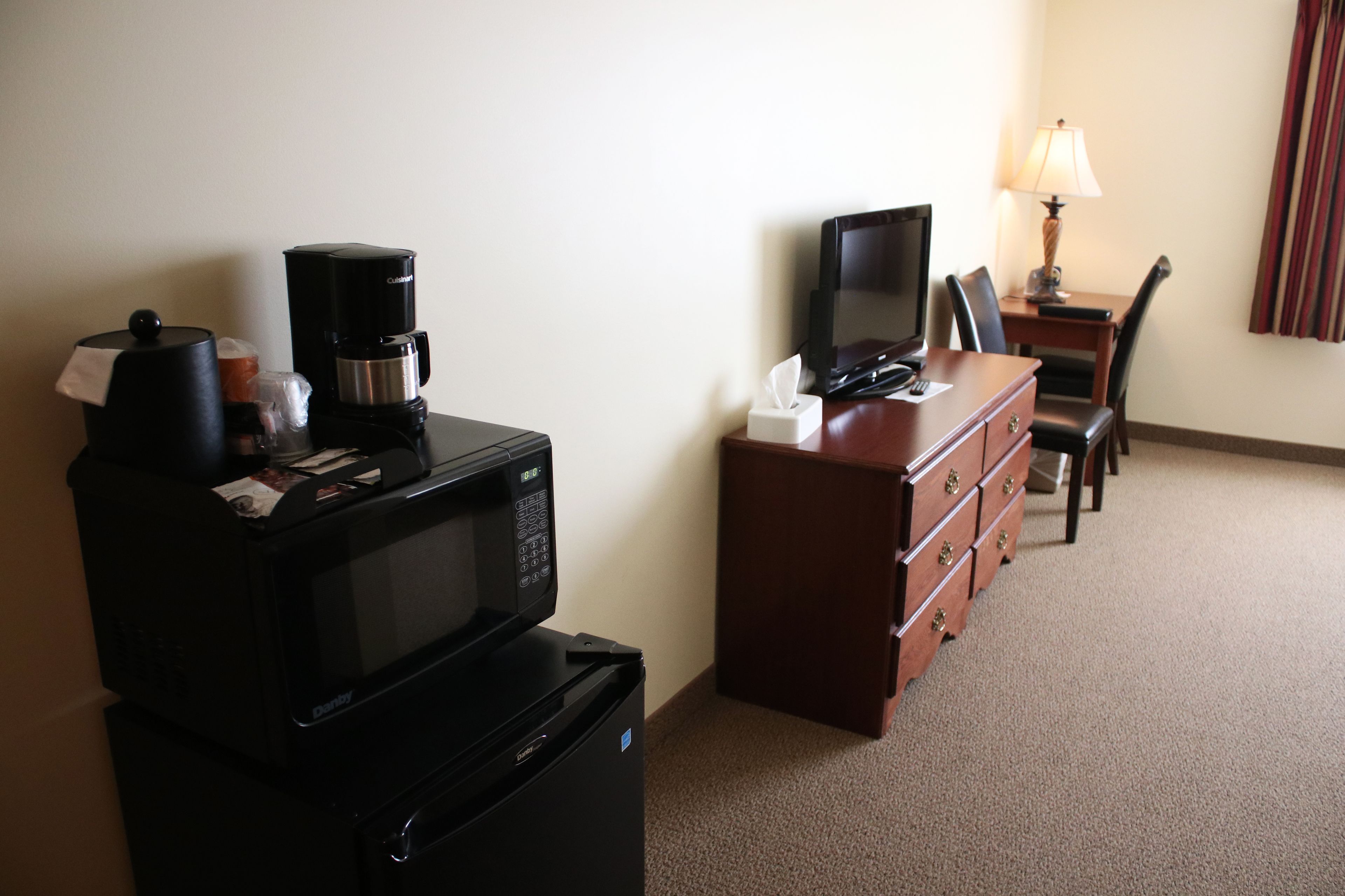 Une chambre d’hôtel compacte comprenant un coin cuisine, une télévision, un bureau avec une lampe et une chaise.