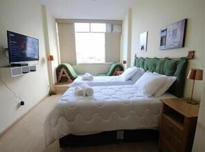 A bedroom with a bed, a television, a window, and a green chair. - Copacabana 1007 (Rio de Janeiro)