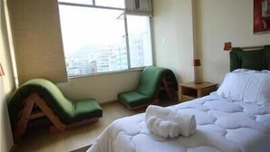A hotel room with a bed, a green armchair, a nightstand, and a window with a view of buildings. - Copacabana 1007 (Rio de Janeiro)