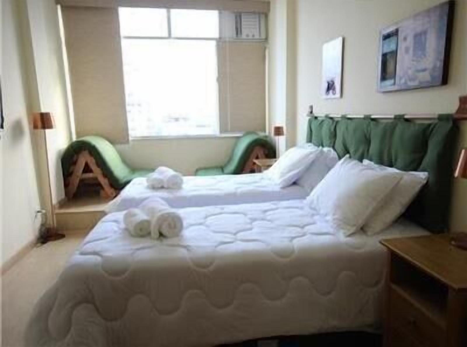 Habitació d'hotel amb un llit, almoines, un capçal de llit verd, una finestra i un quadre a la paret.
