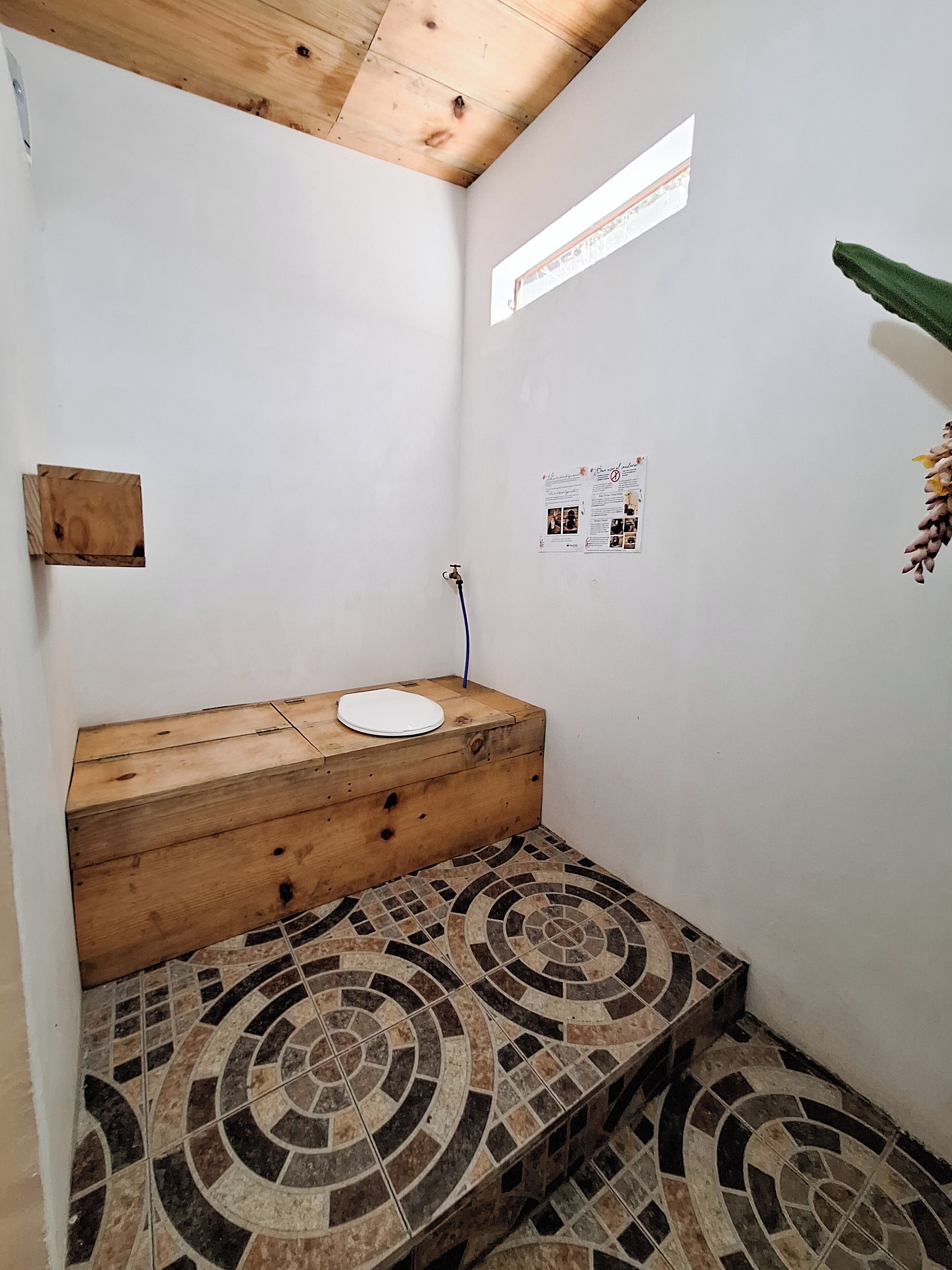 A small, enclosed bathroom with a wooden bench, a white sink, and a tiled floor.