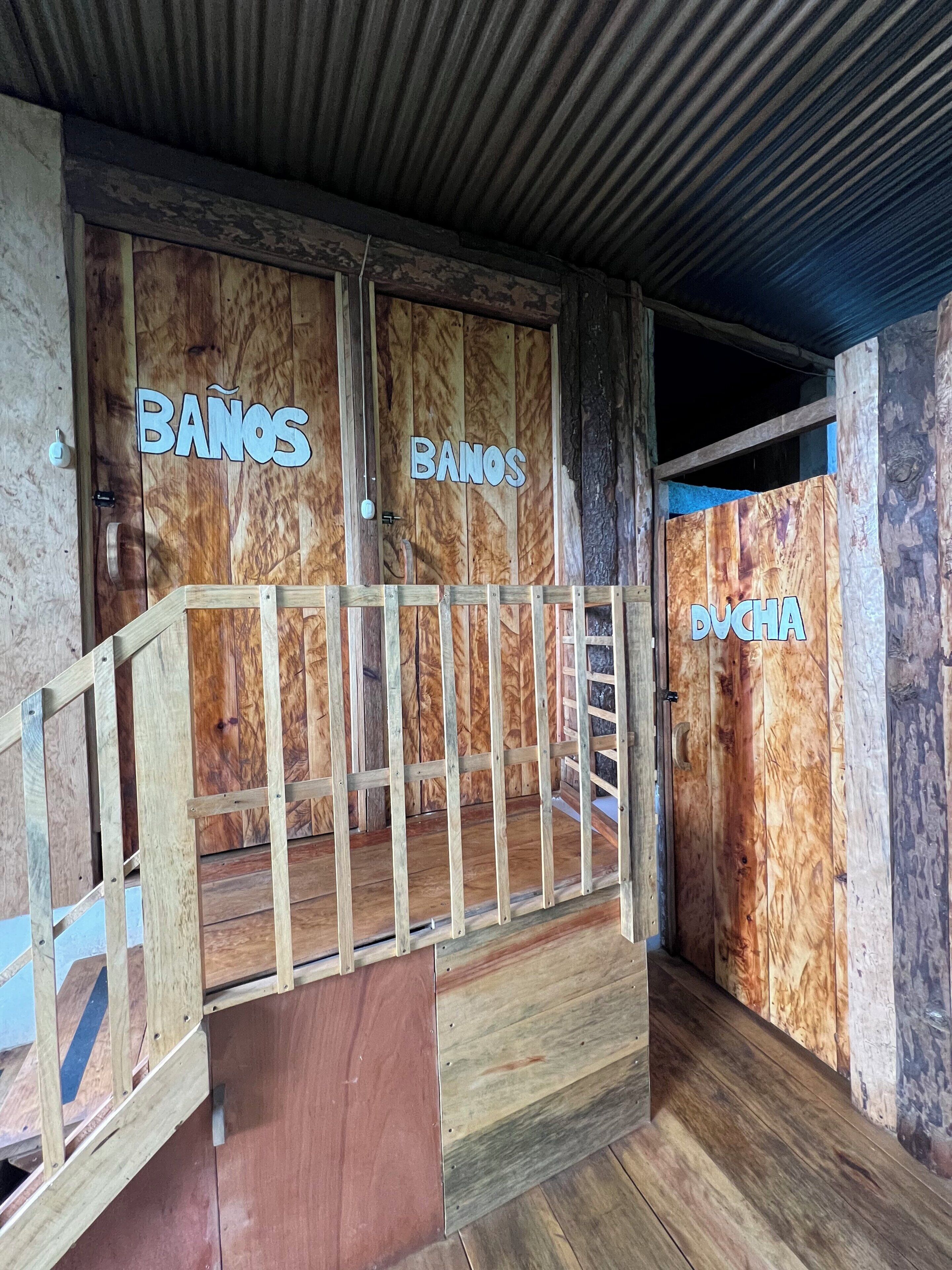 Una struttura in legno con due porte che riportano le scritte 'BANOS' e 'RUCHA'.