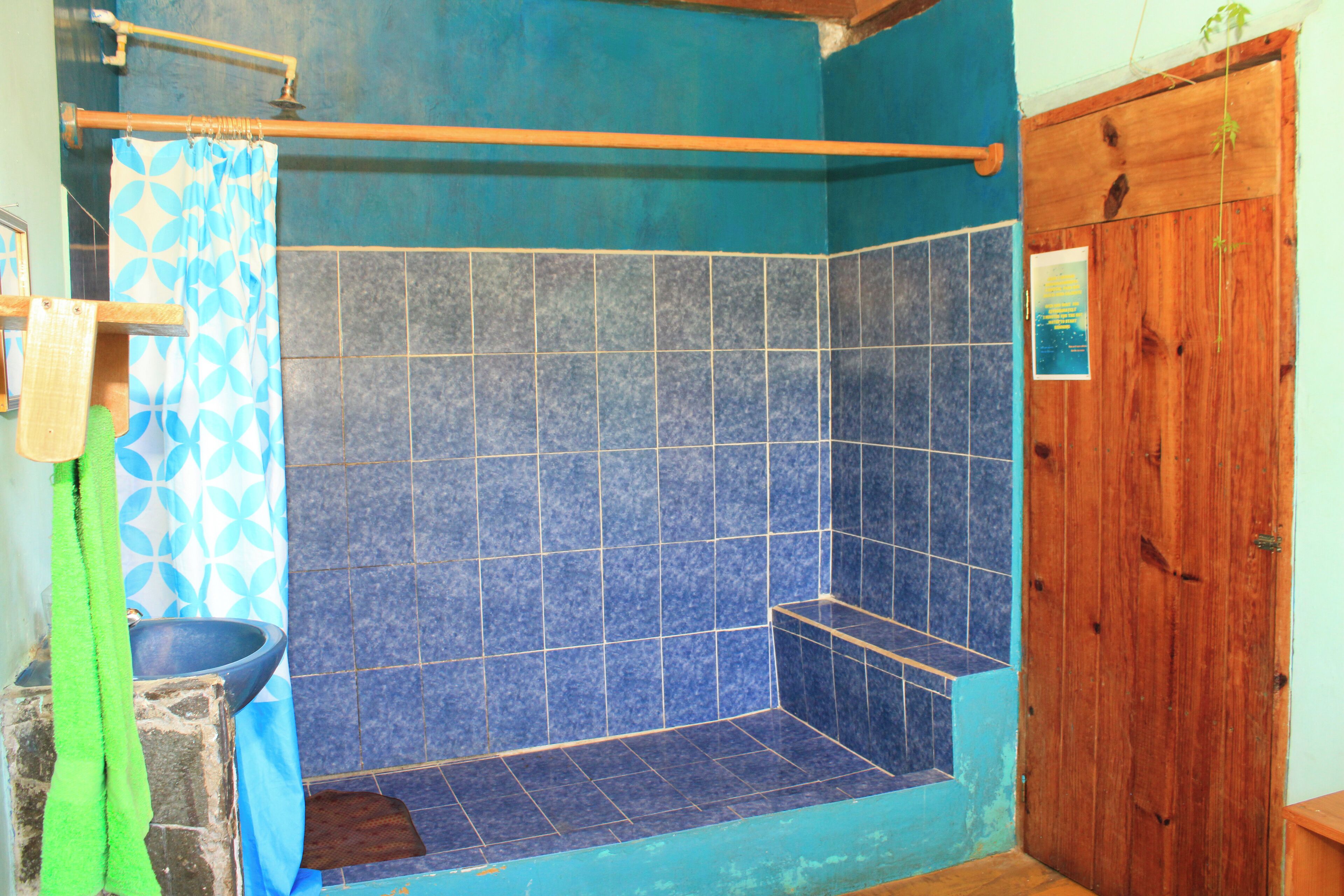 A bathroom with blue tiles, a wooden door, and a shower area with a blue and white patterned curtain.