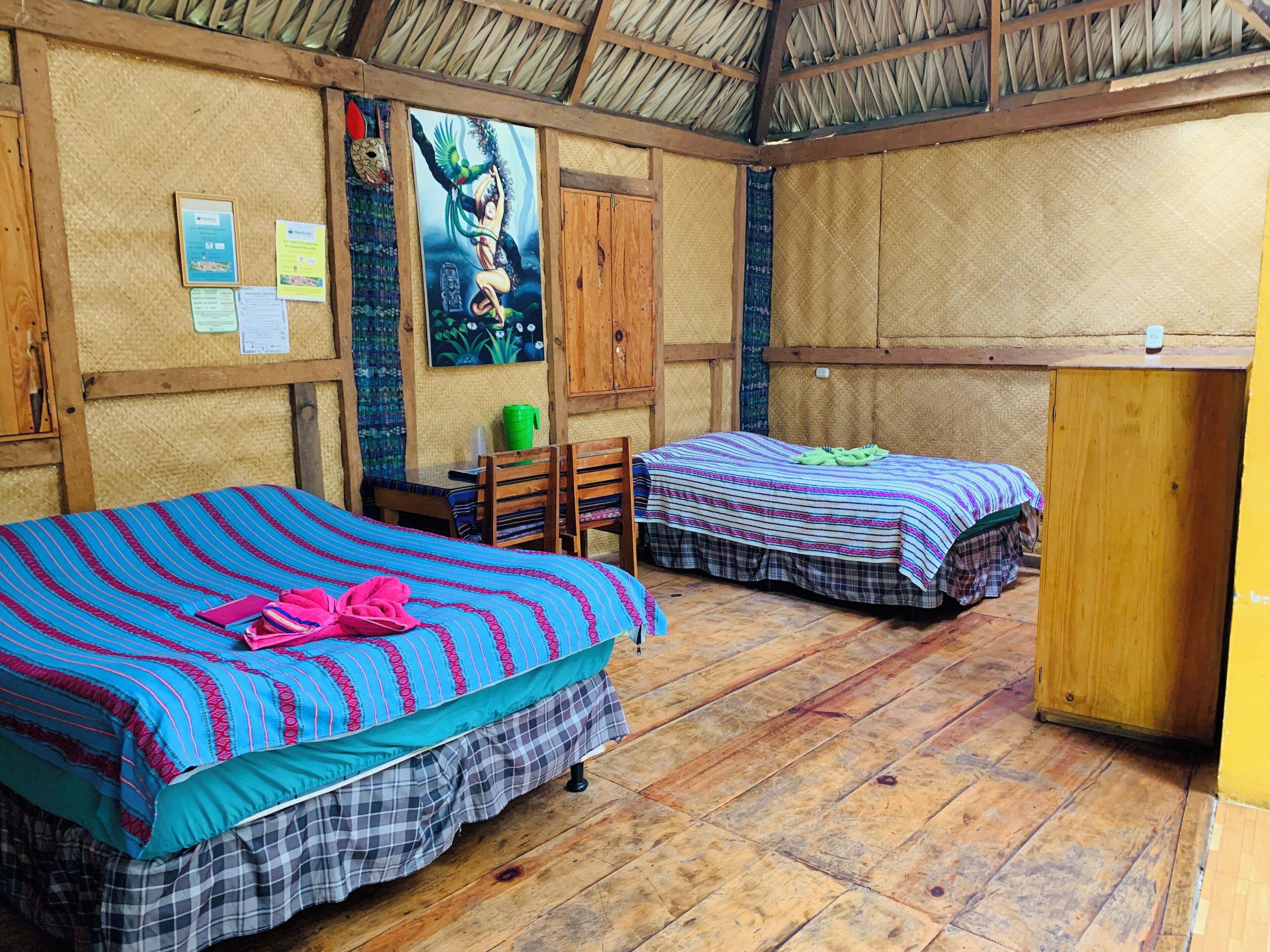 A room with two beds, wooden furniture, and a thatched roof.