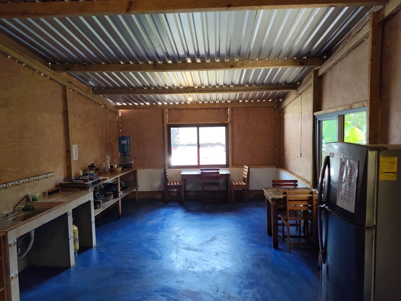 A kitchen with a blue floor, wooden cabinets, a refrigerator, and a window.