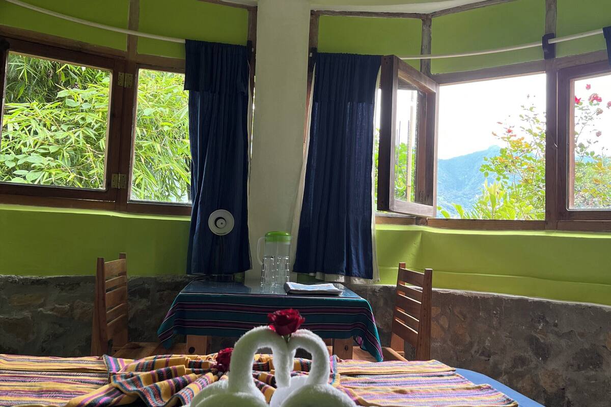 Een kamer met een bed, een tafel met een karaf, en uitzicht op groen buiten.