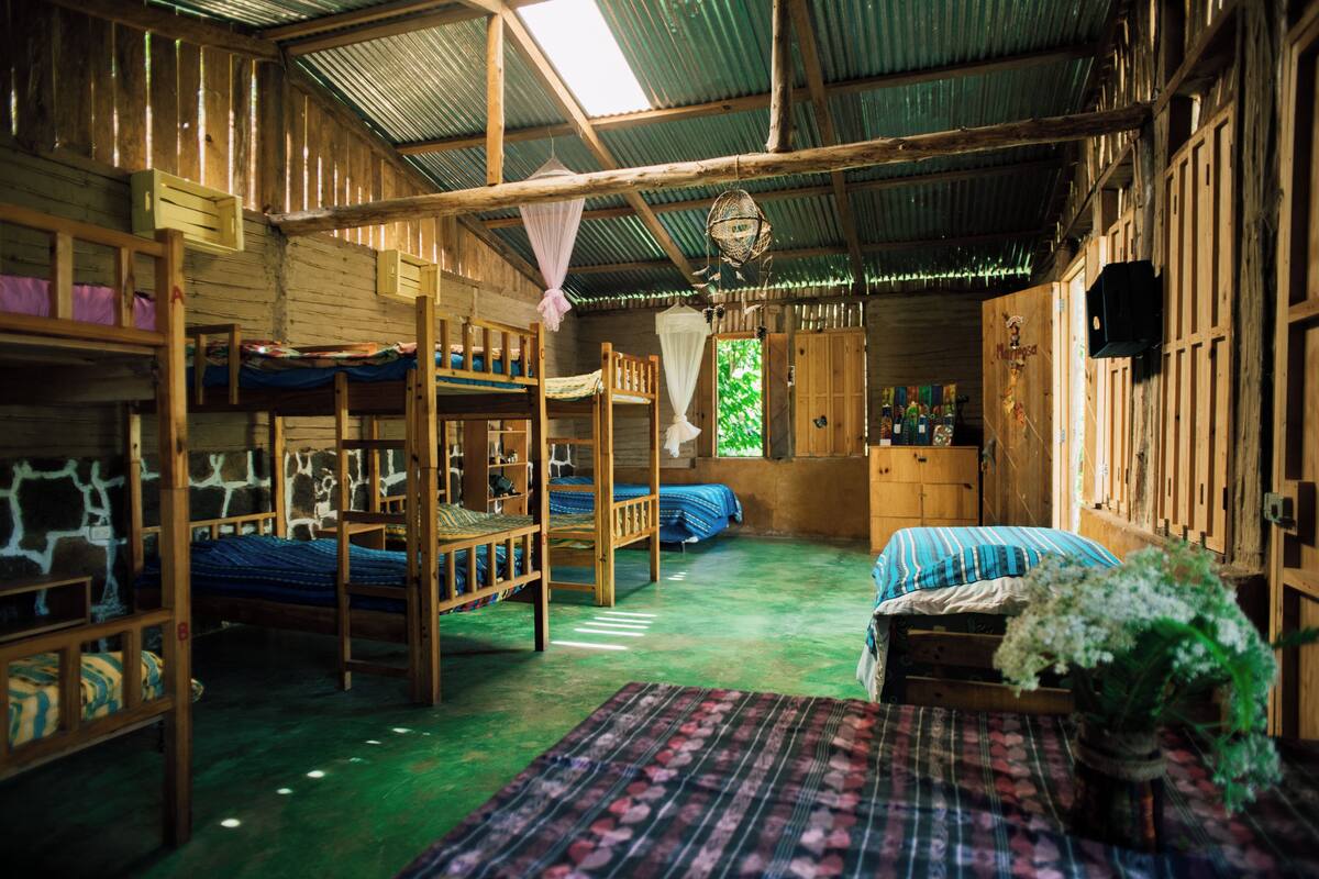 Een rustieke houten hut met stapelbedden, een kleine tafel met een vaas, en een groene vloer.