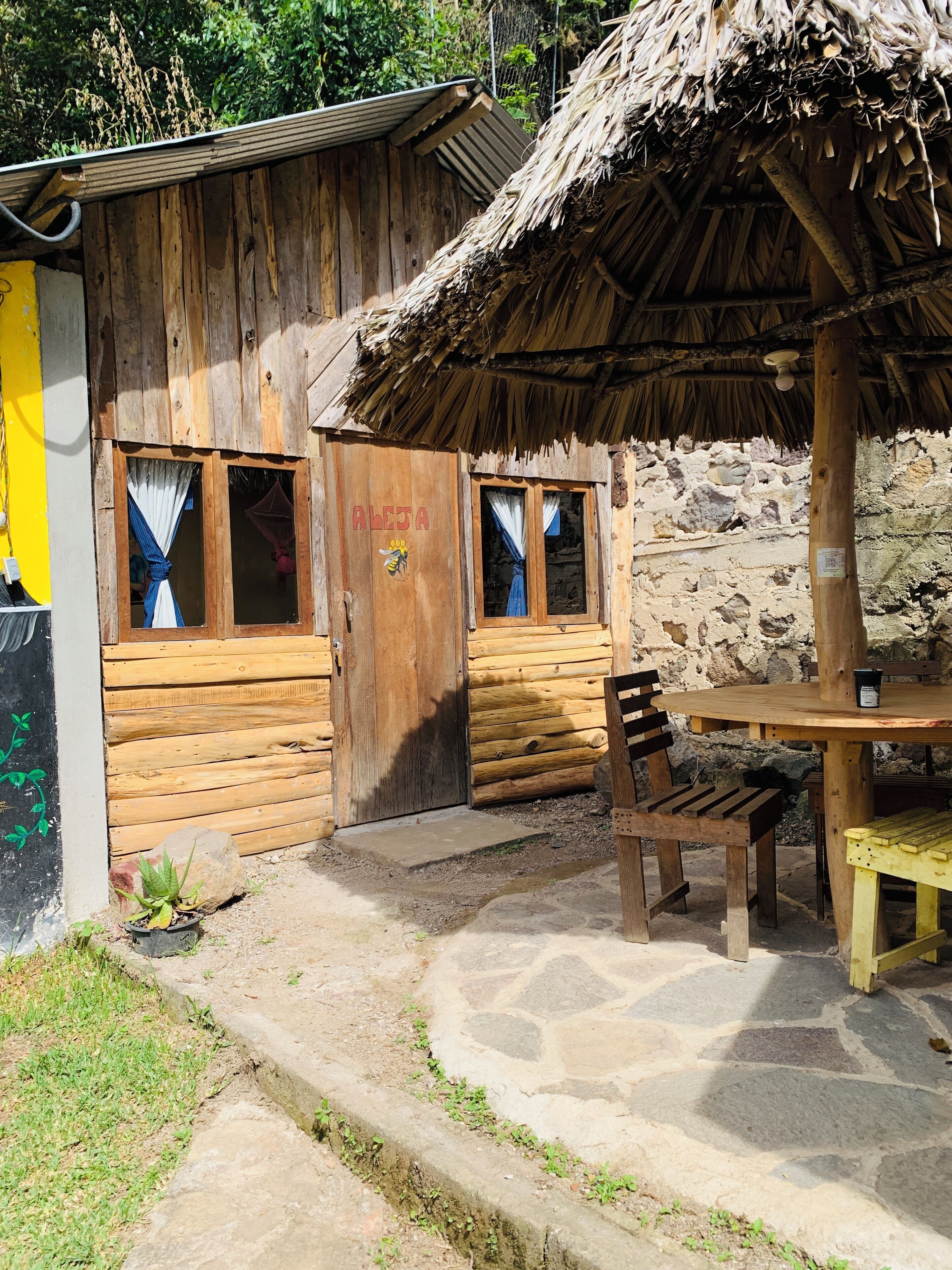 A rustic wooden building with a thatched roof, a bench, and a table.