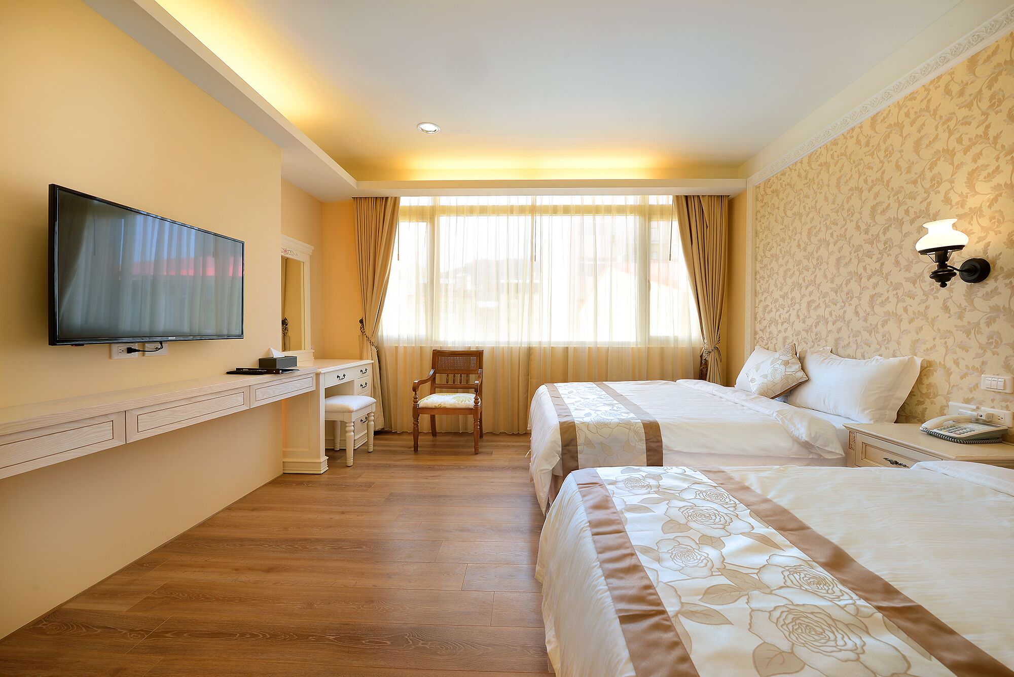 A hotel room with a large bed, a smaller bed, a desk with a chair, a television, and a window with curtains.