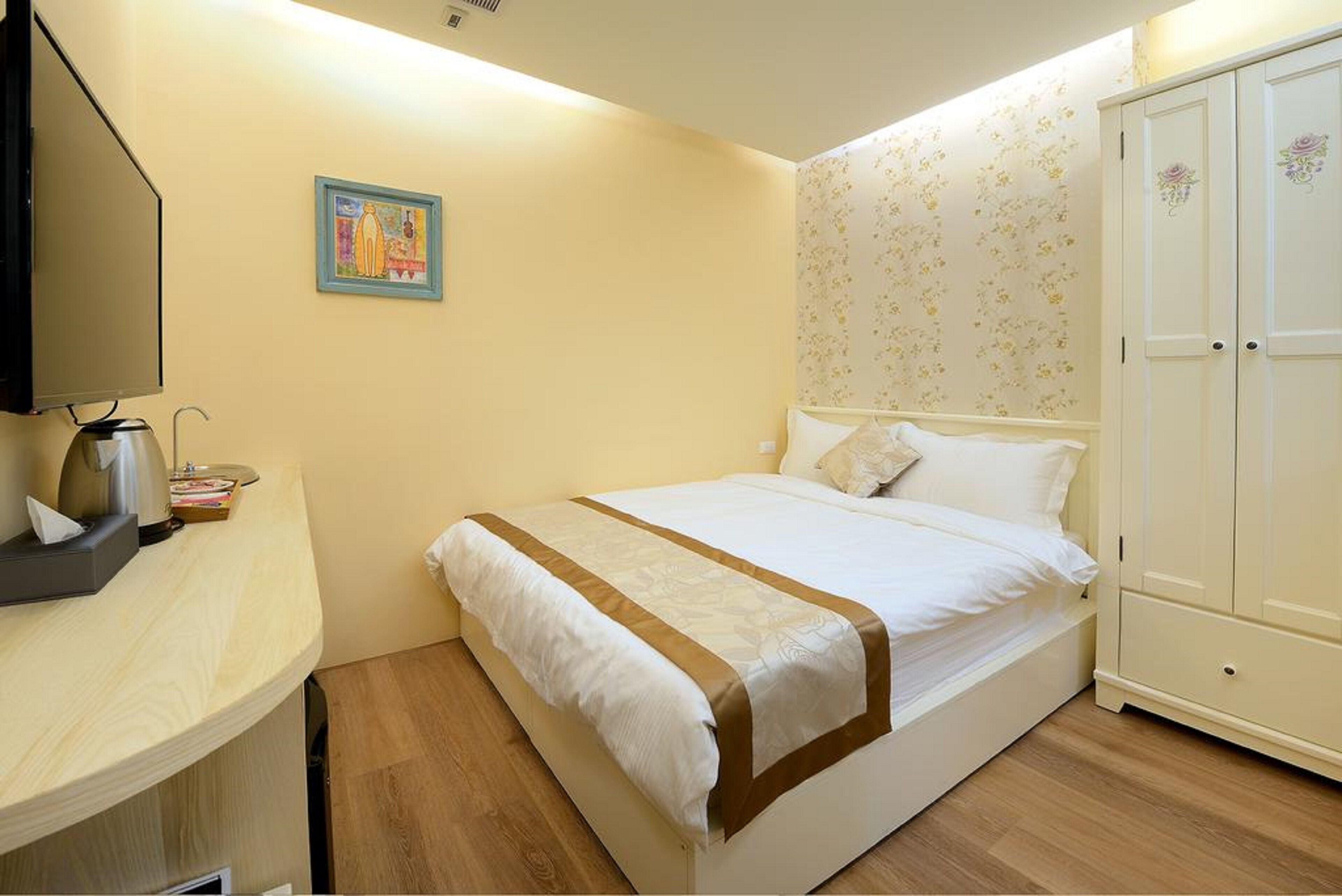 A bedroom with a bed, a bedside table with a lamp, a wardrobe, and a framed picture on the wall.