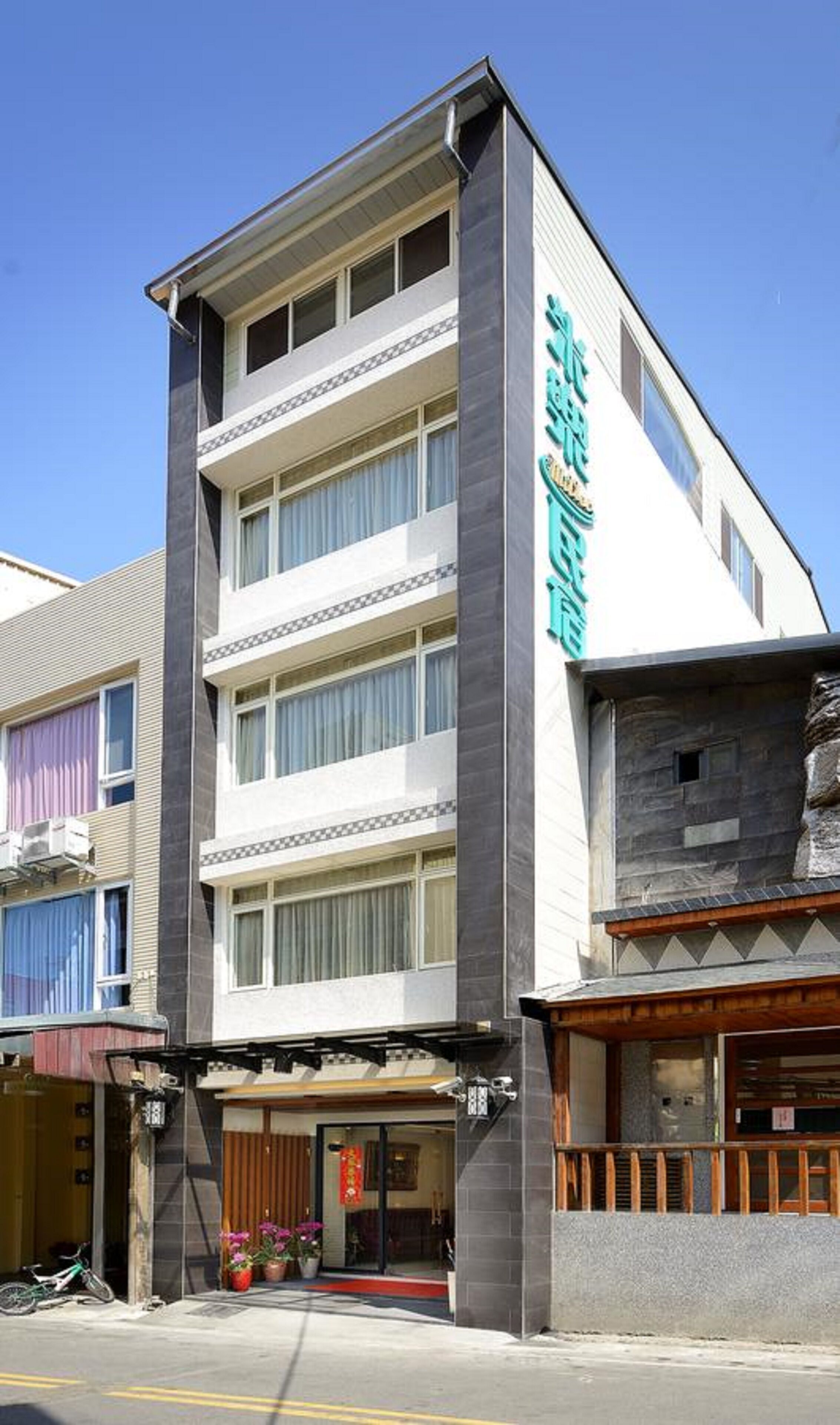 Et hotel i flere etager med en moderne facade, der har en markant indgang med rød løber og plantekasser.