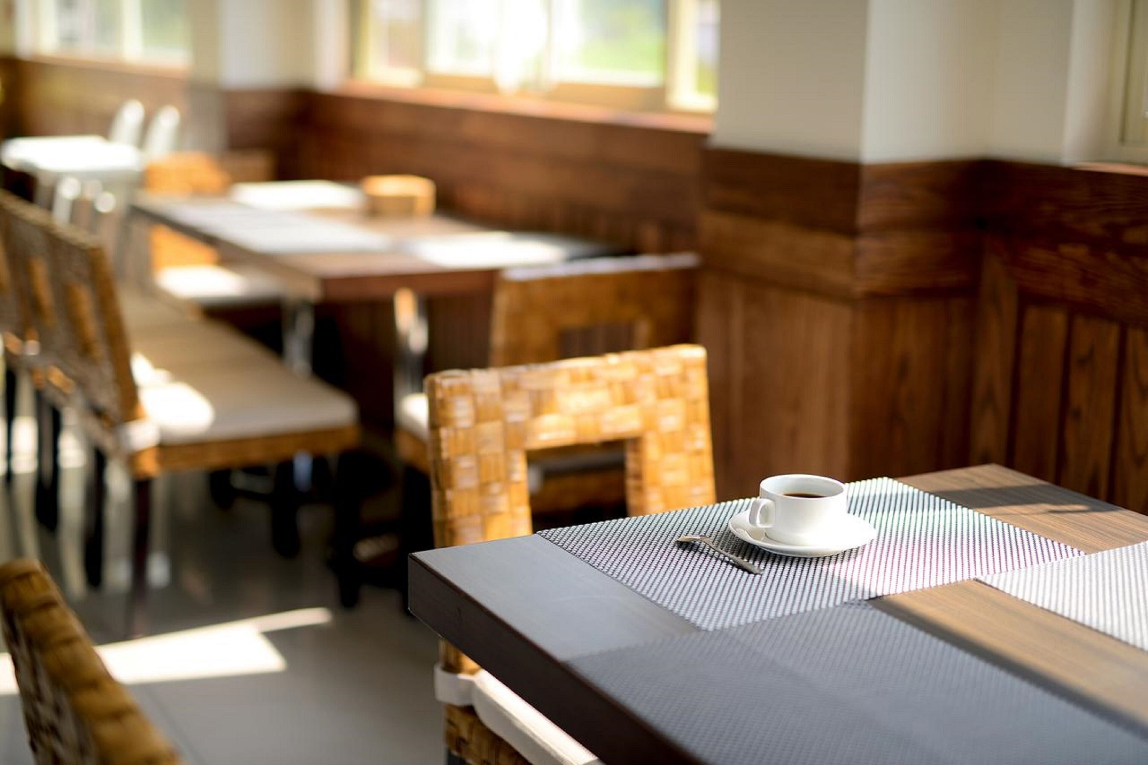 Ein Essbereich mit Holztischen und -stühlen, eine Kaffeetasse auf einem Tisch und ein Fenster, das für natürliches Licht sorgt.