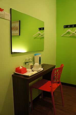 Une petite pièce comprenant un bureau, une chaise, un miroir, une machine à café et quelques effets personnels.