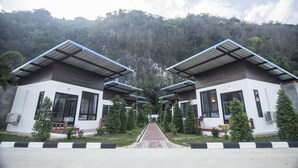A symmetrical building complex with a central pathway leading to a door, surrounded by greenery and a hilly backdrop. - Phuphayot Resort (Huai Yot)
