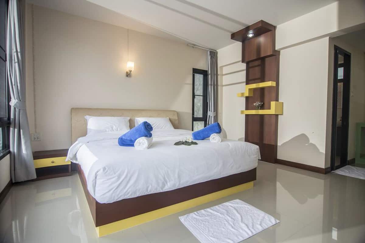 A hotel room with a large bed, a bedside table, a mirror, and a wall-mounted shelf.