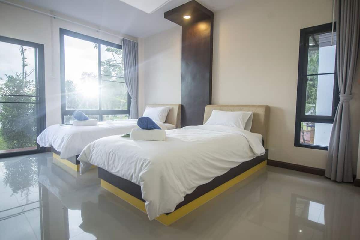 A modern hotel room with two beds, large windows, and a view of greenery.