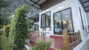 A modern house with large windows, a patio with outdoor furniture, and a lush garden. - Phuphayot Resort (Huai Yot)