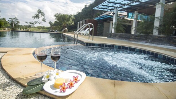A hot tub with a glass-enclosed area, surrounded by palm trees and a pool. - Phuphayot Resort (Huai Yot)