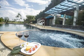 A hot tub with a glass-enclosed area, surrounded by palm trees and a pool. - Phuphayot Resort (Huai Yot)